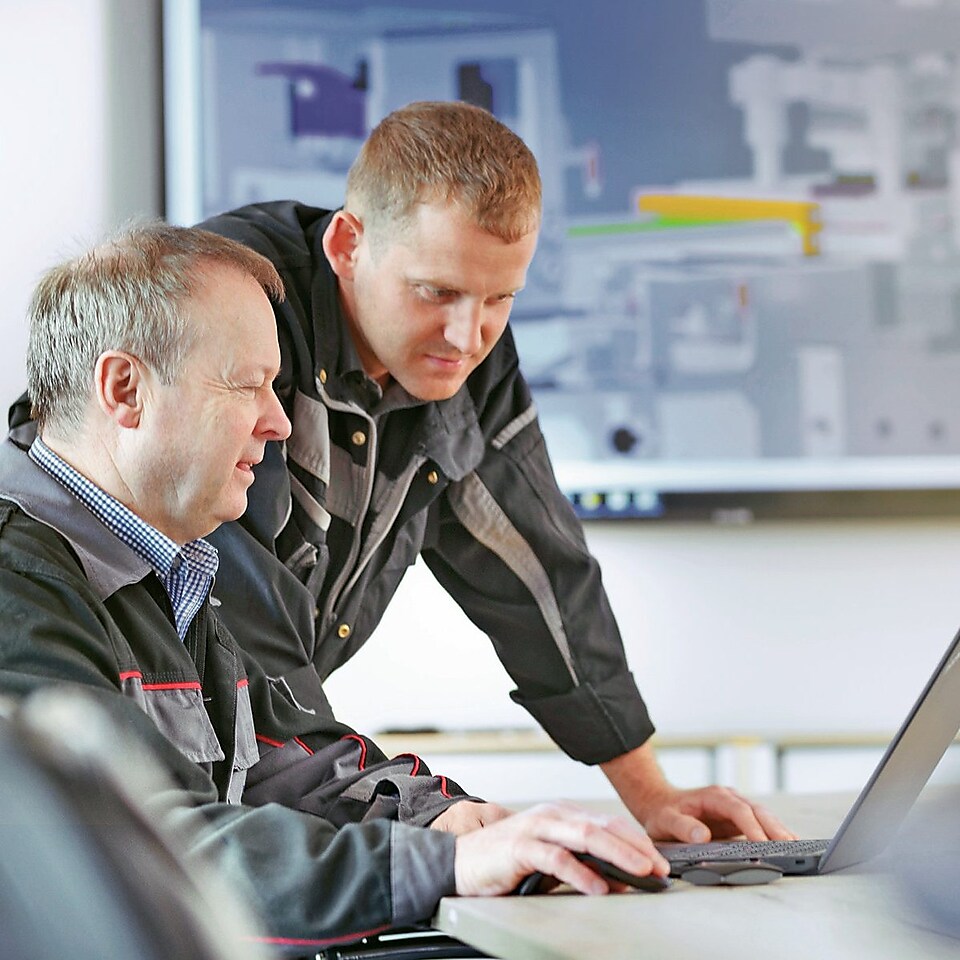 Zwei Männer arbeiten gemeinsam an einem Laptop.