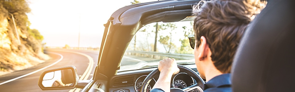 Un jeune homme portant des lunettes de soleil roule vers le soleil dans une voiture décapotable