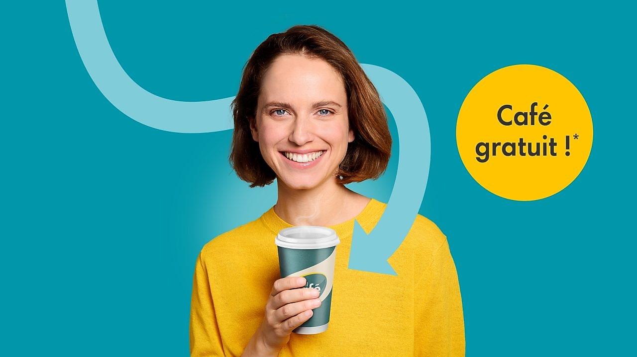 Une jeune femme en pull jaune tient en souriant un gobelet de café Shell Café devant un fond bleu turquoise. À côté d’elle se trouve un cercle jaune avec l’inscription « Café gratuit ! » et une flèche courbée pointe vers le gobelet.