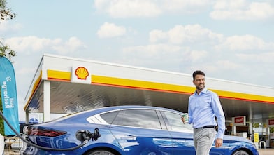 Un homme profite du temps de recharge à la borne de recharge ultra-rapide Shell Recharge pour déguster un café au Shell Café