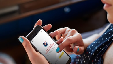 Une femme est assise dans sa voiture et tient un téléphone avec l’application Shell ouverte et Shell SmartPay configuré