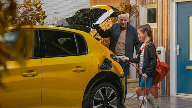 Ein junges Mädchen und ihr Großvater laden ein Elektroauto zu Hause auf