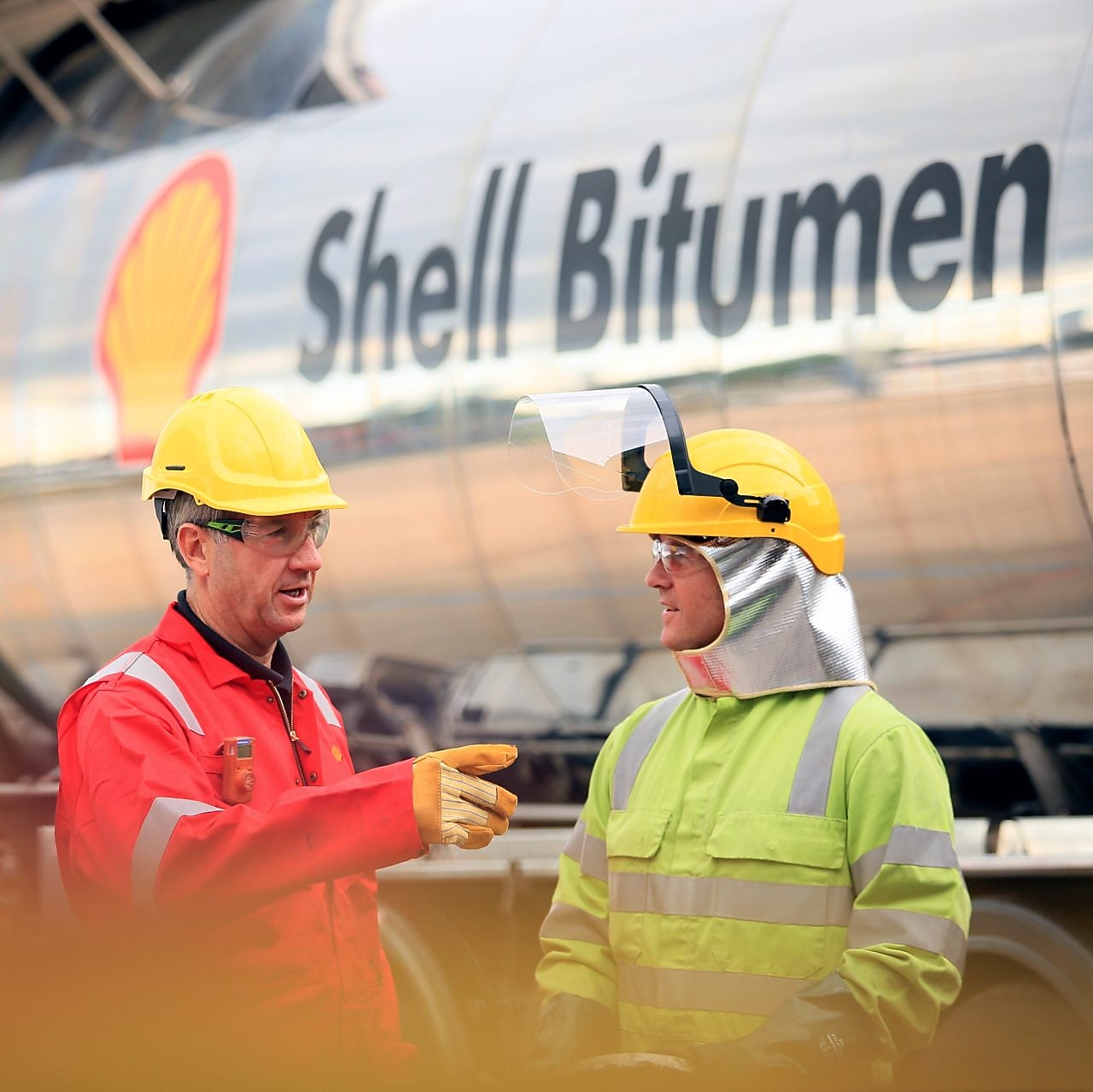 Zwei Mitarbeiter unterhalten sich vor einem Tankwagen mit der Aufschrift "Shell Bitumen"