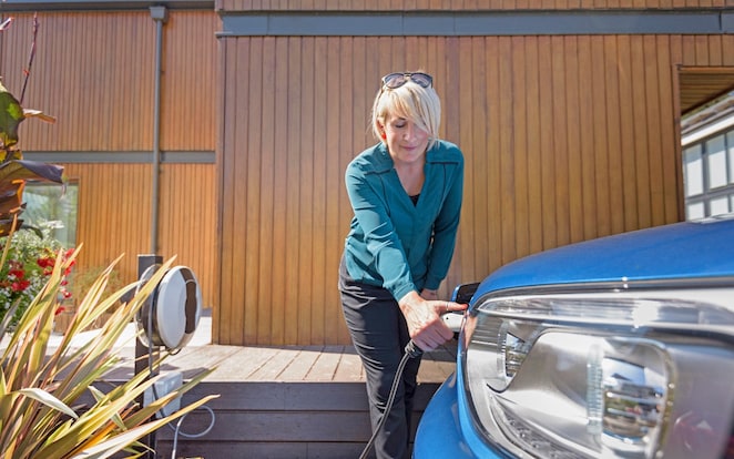 Eine Frau steht neben ihrem E-Auto und beginnt mit dem Laden.