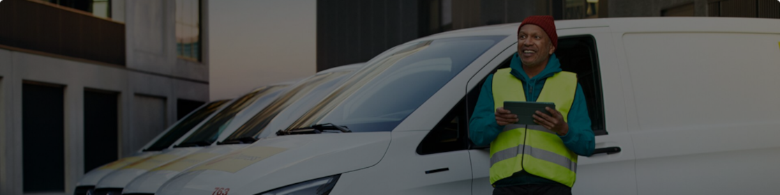Ein Mann steht mit einem Tablet in der Hand vor mehreren E-Transportern, die aufgeladen werden