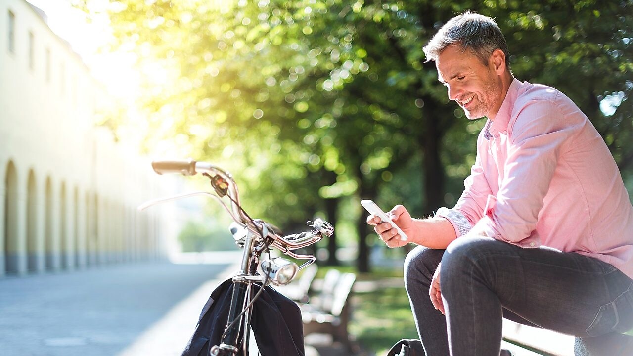 Ein Flottenmanager sitzt entspannt auf einer Parkbank mit seinem Smartphone in der Hand. Davor steht sein Fahrrad.