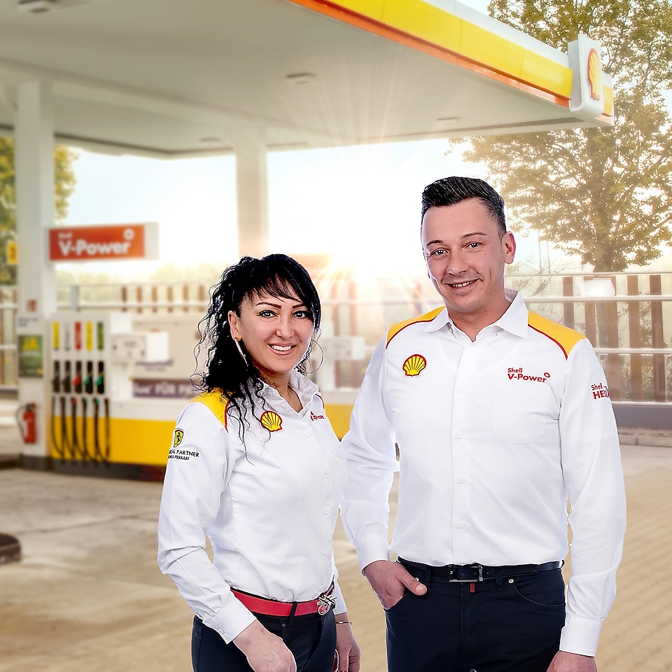 Zwei Mitarbeiter in Shell Dienstkleidung stehen auf einer Shell Tankstelle