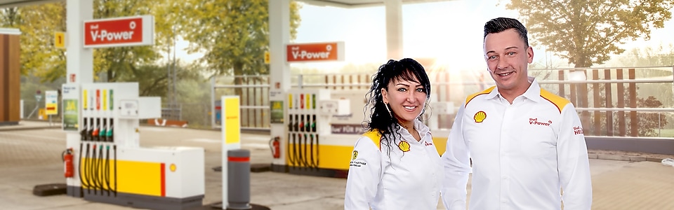 Zwei Mitarbeiter in Shell Dienstkleidung stehen auf einer Shell Tankstelle