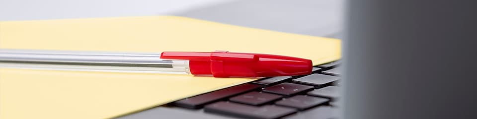 Roter Kugelschreiber und gelbes Blatt Papier auf der Tastatur eines Laptops