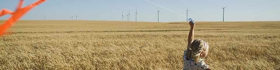 Mädchen in einem Kornfeld lässt Drachen steigen, Windräder im Hintegrund