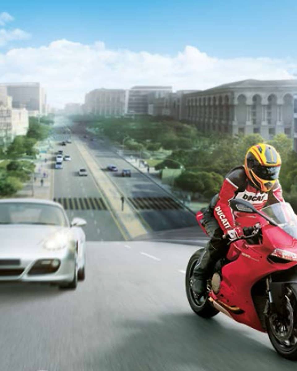 Rotes Motorrad und Fahrer auf einer Straße mit Autos und Gebäuden im Hintergrund.