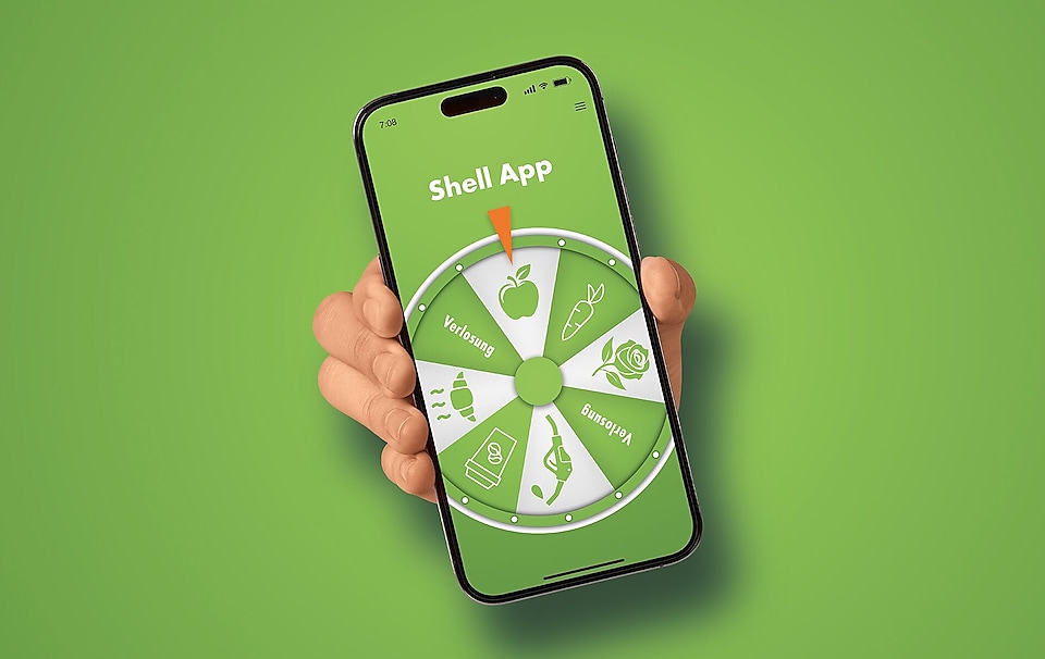 Hand präsentiert Smartphone mit Glücksrad-Screen vor grünem Hintergrund. 