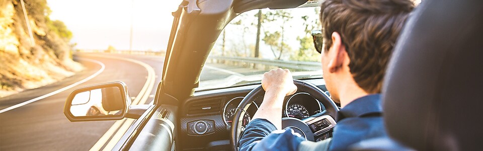 Junger Mann mit Sonnenbrille fährt im Cabrio der Sonne entgegen