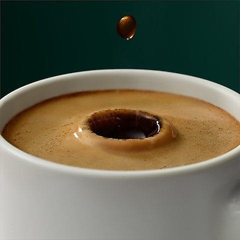 Eine Tasse Kaffee in den mittig ein Tropfen hineinfällt