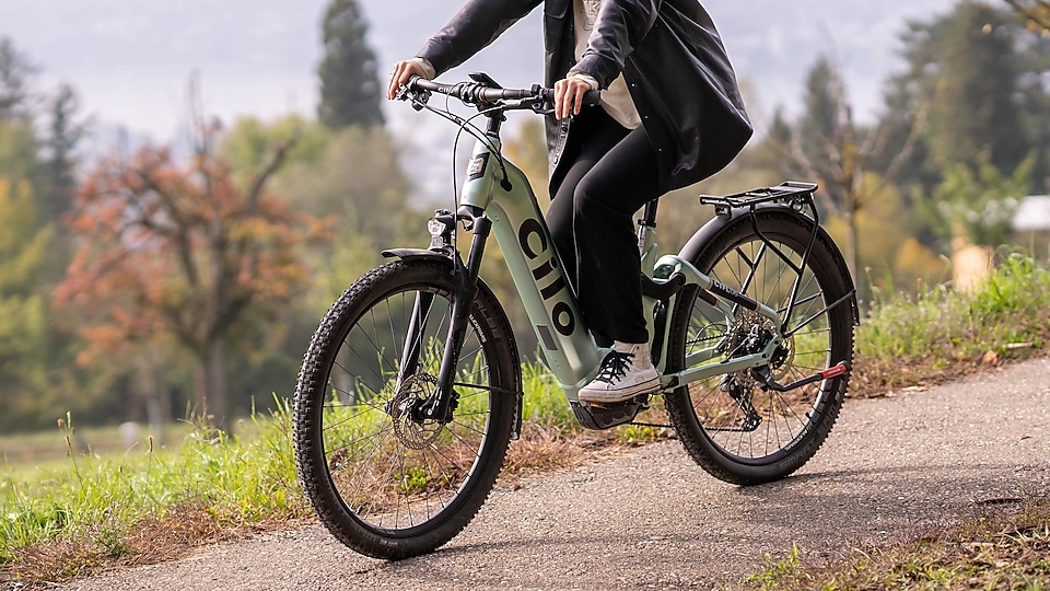 Ein Mann befährt mit einem Cilo Bike einen geschotterten Weg neben einer Wiese