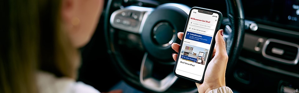 Frau im parkenden Auto sitzt hinter dem Steuerrad und schaut auf ihr Smartphone.