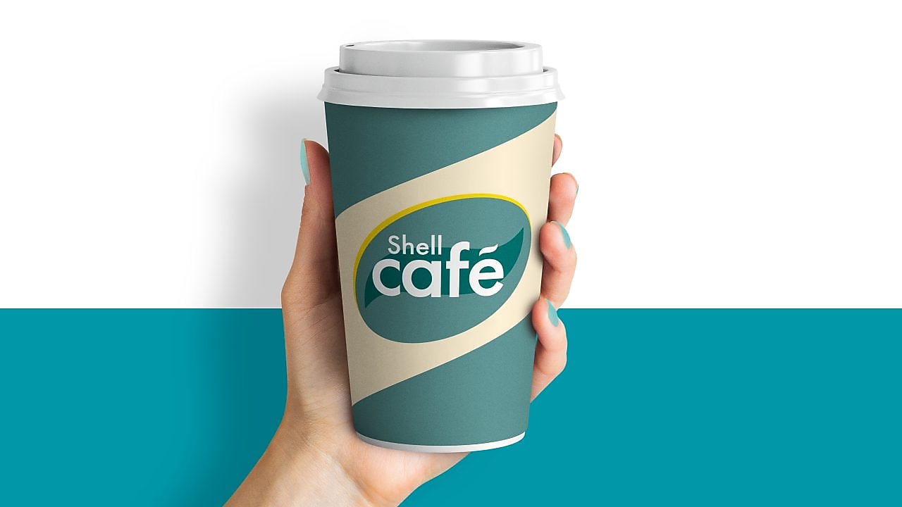 Hand hält einen Shell Café Kaffee Becher vor weiß-türkisem Grund.
