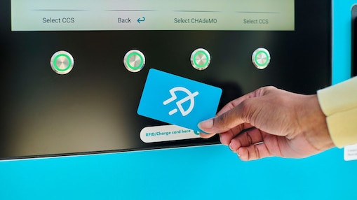 Eine Hand hält eine türkisfarbene Shell Recharge Ladekarte vor ein Kartenlesegerät einer Ladesäule. Auf dem Display im Hintergrund sind verfügbare Ladepunkte mit den Optionen CCS und CHAdeMO zu sehen.