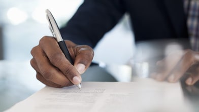 Nahaufnahme einer Hand, die mit einem Stift auf ein Dokument schreibt.