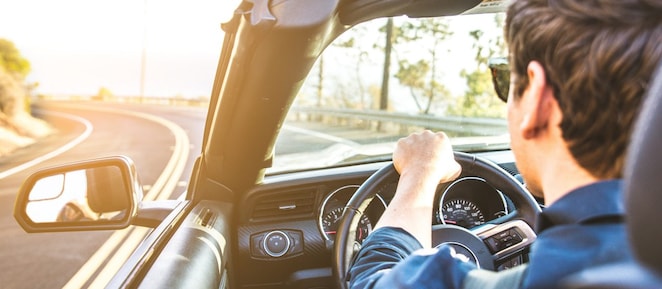 Junger Mann mit Sonnenbrille fährt im Cabrio der Sonne entgegen