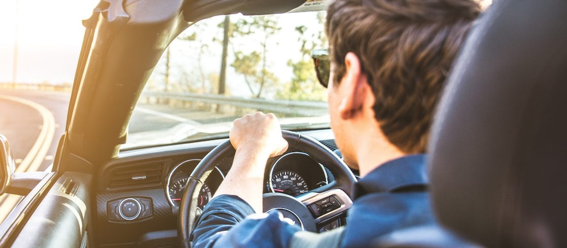 Junger Mann mit Sonnenbrille fährt im Cabrio der Sonne entgegen