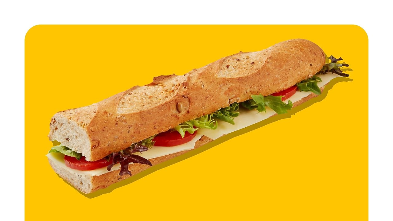 Halbes Baguette-Sandwich mit Käse, Salat und Gurken auf gelbem Hintergrund.