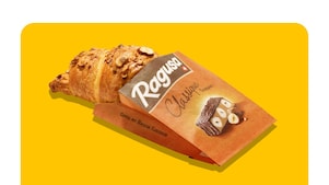 Croissant mit Nuss-Nougat-Füllung in Papiertüte, Aufschrift „Ragusa Classique Croissant“ und „Gipfel mit Ragusa Classique“ auf gelbem Hintergrund.