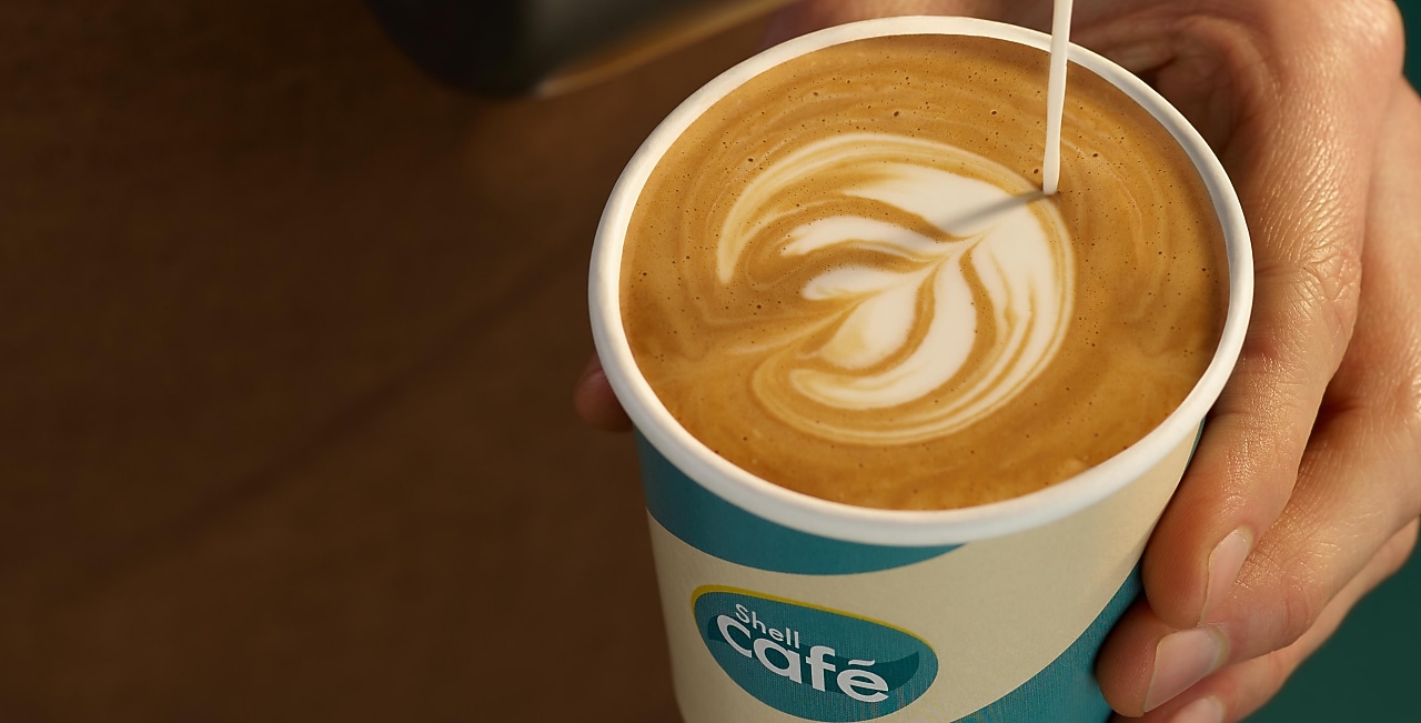 Barista schenkt Milchkaffee in einen Shell Café Becher ein