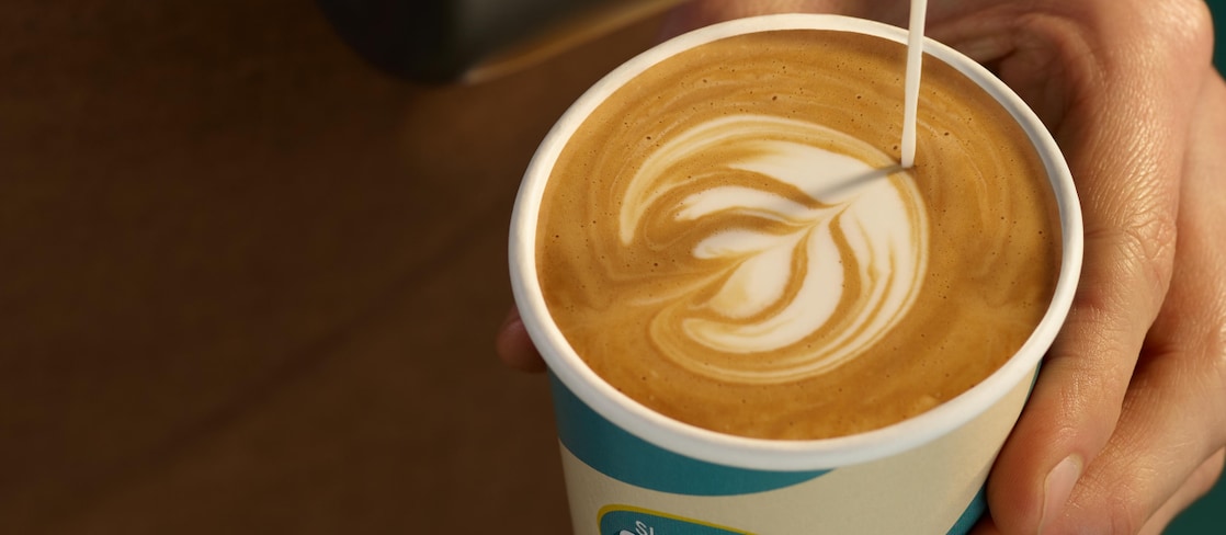 Barista schenkt Milchkaffee in einen Shell Café Becher ein