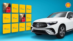 SUV Mercedes blanc à droite de l’image, à gauche un jeu de memory Shell Car Wash avec des cartes jaunes montrant des scènes de lavage auto sur fond bleu, avec le logo Shell dans le coin supérieur droit.