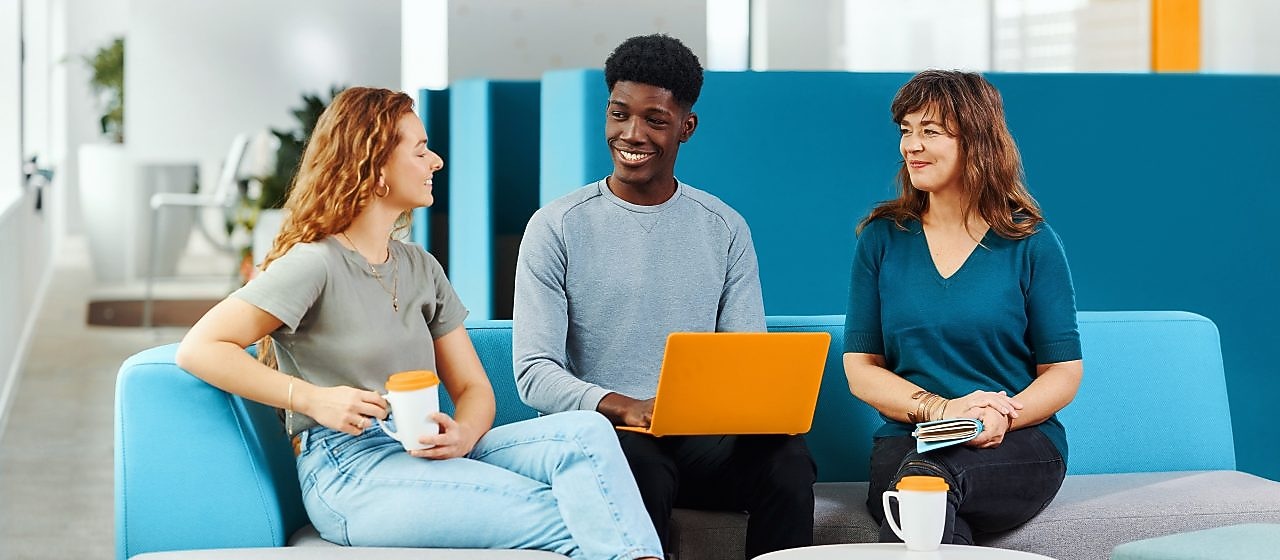 Trois personnes dans un bureau bien éclairé, l’une avec un ordinateur portable, une autre avec une tasse de café