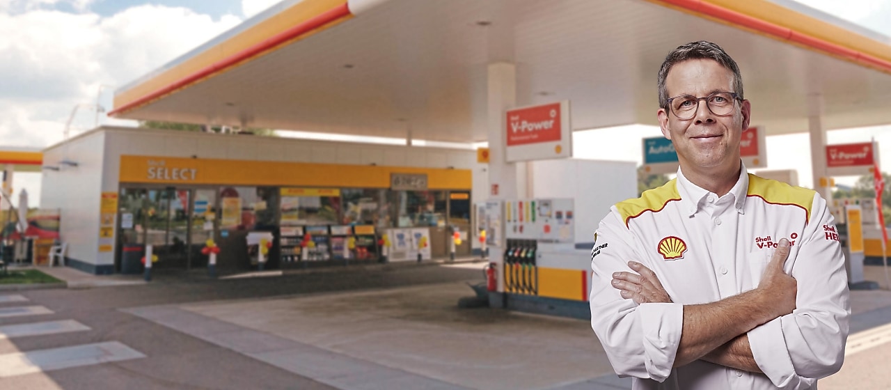 Gérant de station-service Shell devant une station Shell