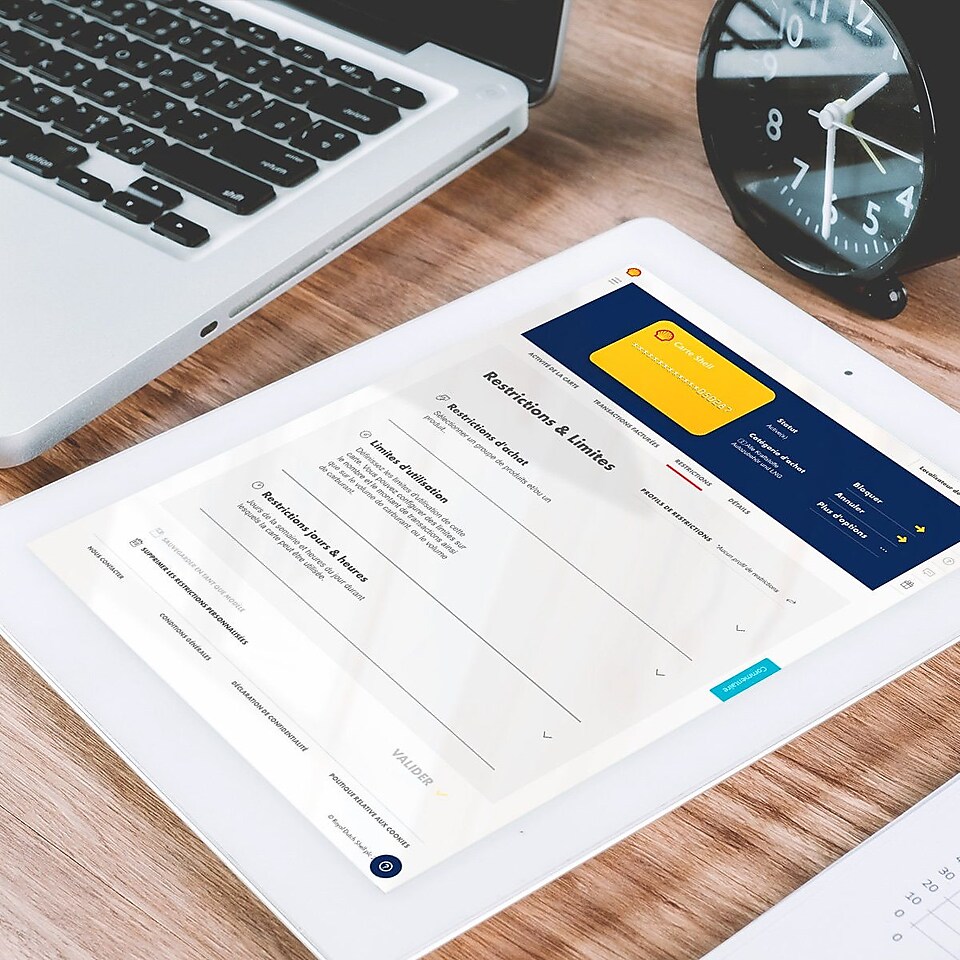 Une tablette se trouve sur une table à côté d'un ordinateur portable. Sur la tablette, on voit les fonctions de restriction du Shell Fleet Hub.