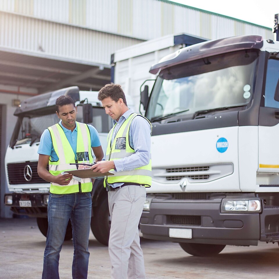 Deux hommes sont debout près d'un camion et regardent une tablette.