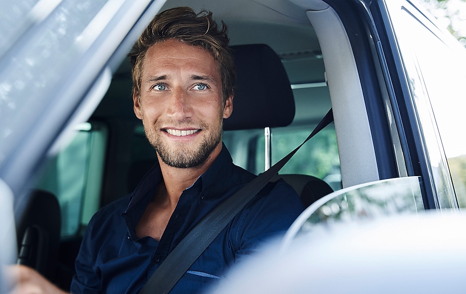 Ein mann sitzt in einem Auto und grinst.