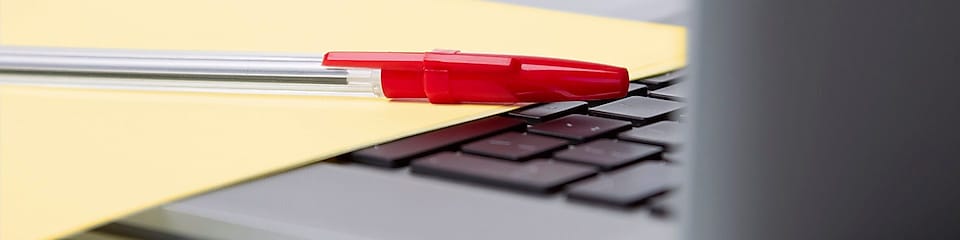 Stylo rouge et feuille de papier jaune sur le clavier d’un ordinateur portable.