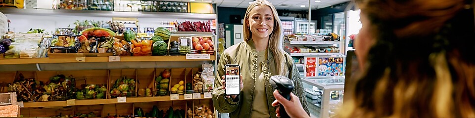 Une main tenant un téléphone portable apparaît, déchirant une toile de papier jaune. L’écran affiche « La nouvelle application Shell % ». Juste à gauche du téléphone portable se trouve une flèche rouge avec 4 icônes : pistolet distributeur, gobelet à café, installation de lavage et trois points (et bien plus encore...)