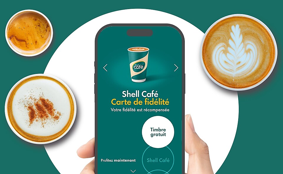 Un téléphone portable tenu par une main, montrant la carte de fidélité Shell Café, avec en arrière-plan des tasses de café vues d’en haut.