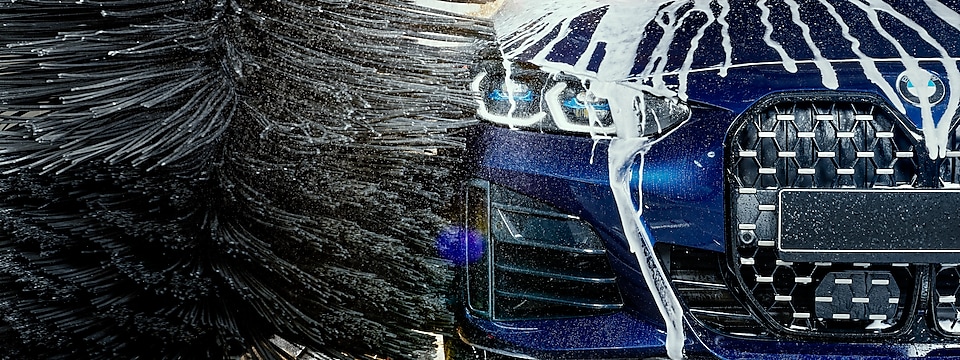 Blaues Auto der Marke BMW in der Waschanlage, über welches Schaum läuft.