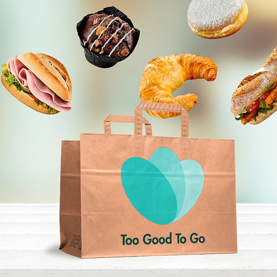 Sac en papier Too Good To Go avec des snacks qui flottent au-dessus, comme un croissant et un muffin.
