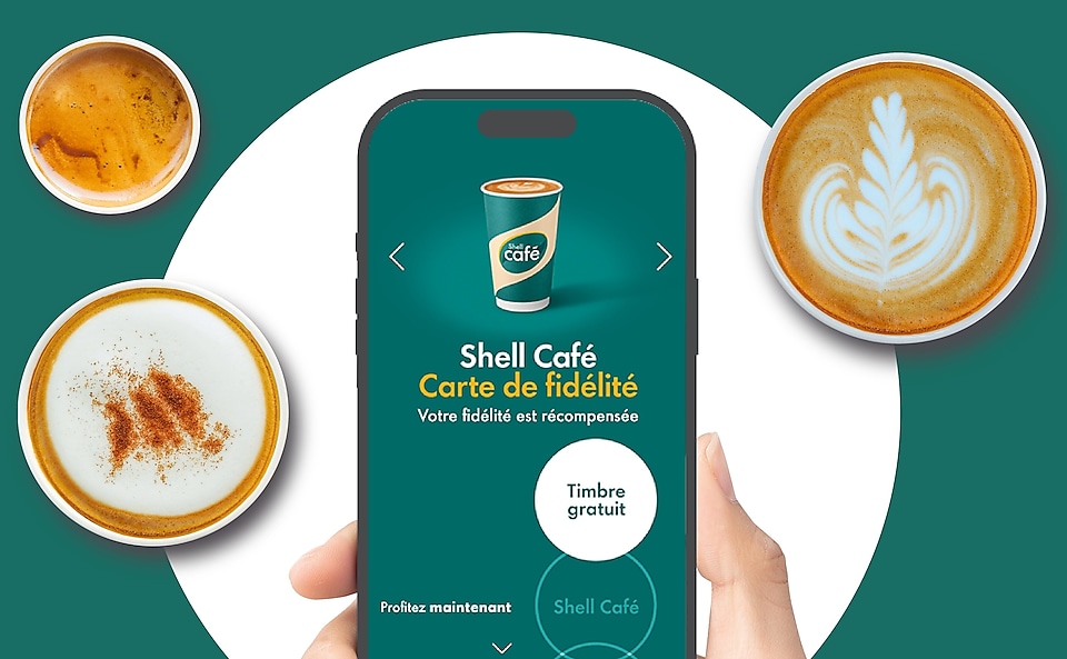 Un téléphone portable tenu par une main, montrant la carte de fidélité Shell Café, avec en arrière-plan des tasses de café vues d’en haut.