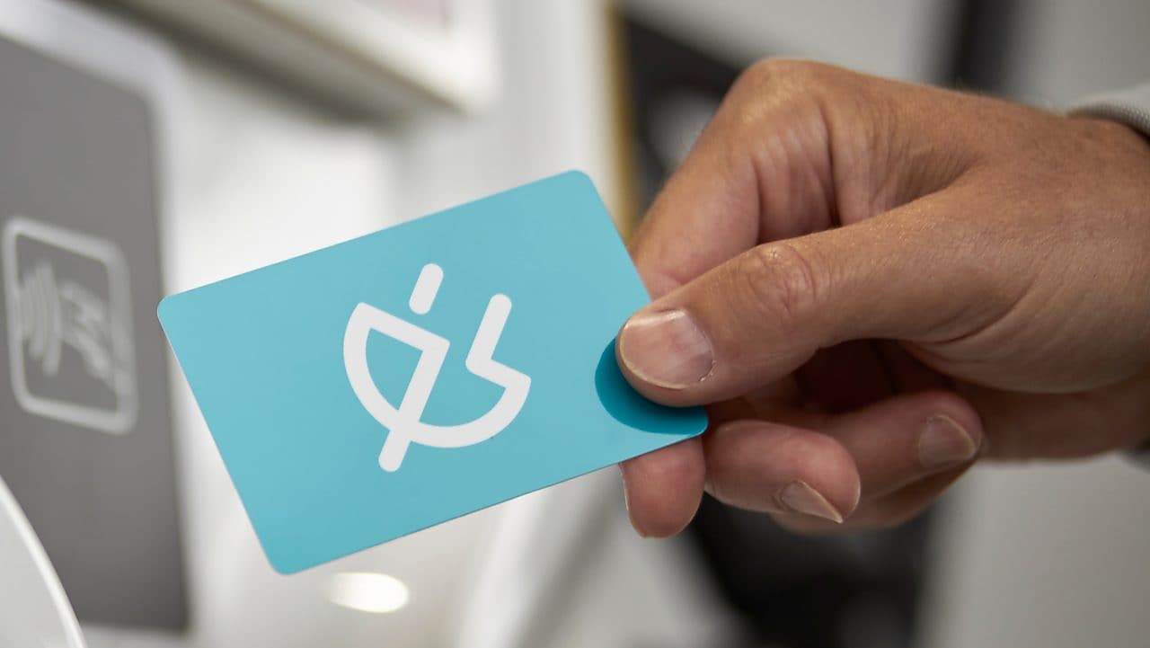 Une main tient un gobelet de café Shell sur un fond turquoise. Texte sur encart jaune&nbsp;: Boisson chaude GRATUITE.