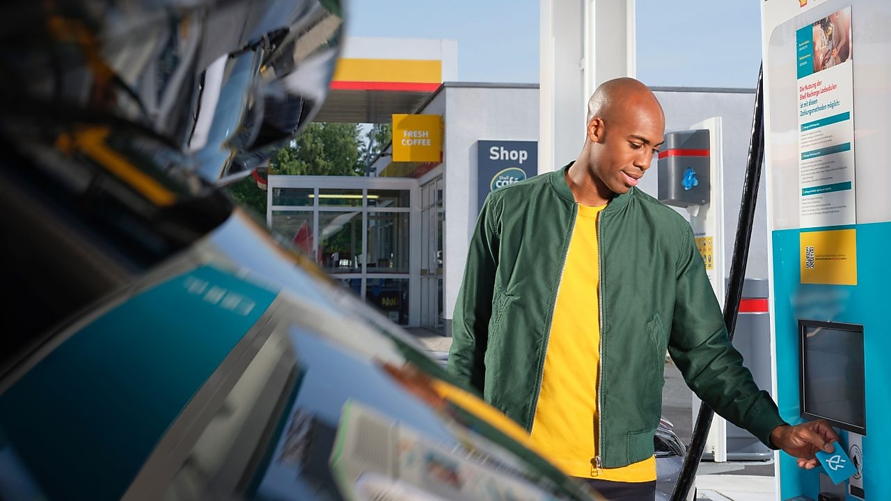 Une main tient un gobelet de café Shell sur un fond turquoise. Texte sur encart jaune&nbsp;: Boisson chaude GRATUITE.