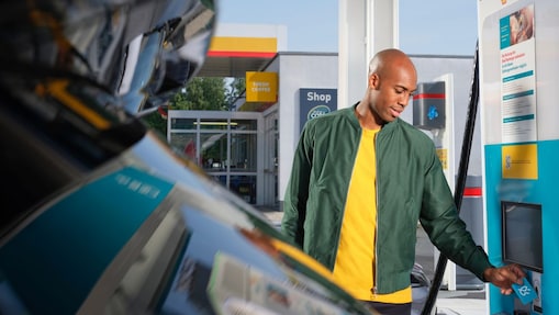 Une main tient un gobelet de café Shell sur un fond turquoise. Texte sur encart jaune&nbsp;: Boisson chaude GRATUITE.