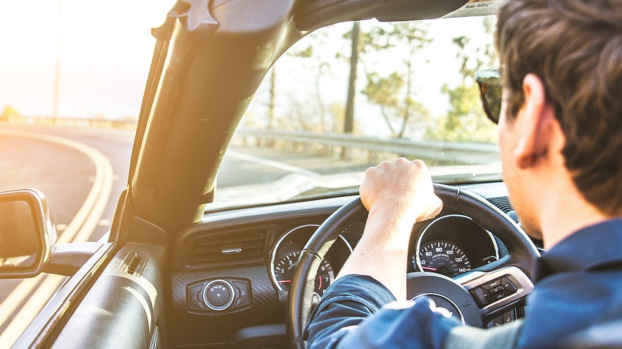 Un jeune homme avec des lunettes de soleil se dirige vers le soleil dans un cabriolet