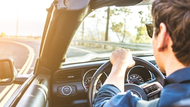 Un jeune homme avec des lunettes de soleil se dirige vers le soleil dans un cabriolet