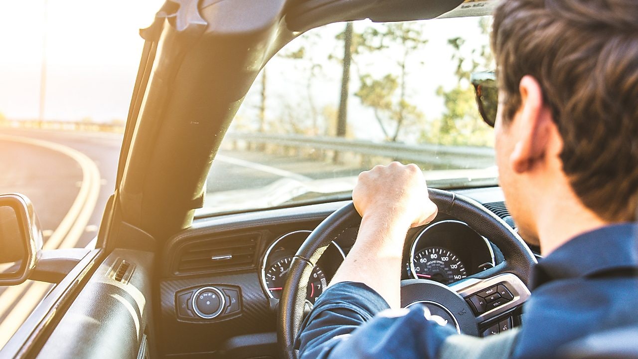 Un jeune homme avec des lunettes de soleil se dirige vers le soleil dans un cabriolet