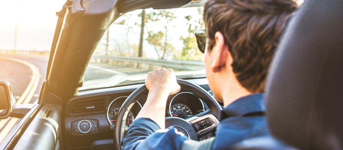 Un jeune homme avec des lunettes de soleil se dirige vers le soleil dans un cabriolet