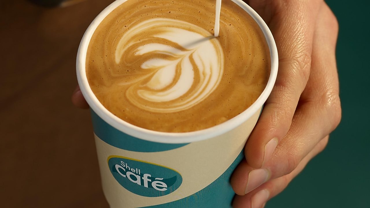 Un barista sert un café au lait dans un gobelet Shell Café