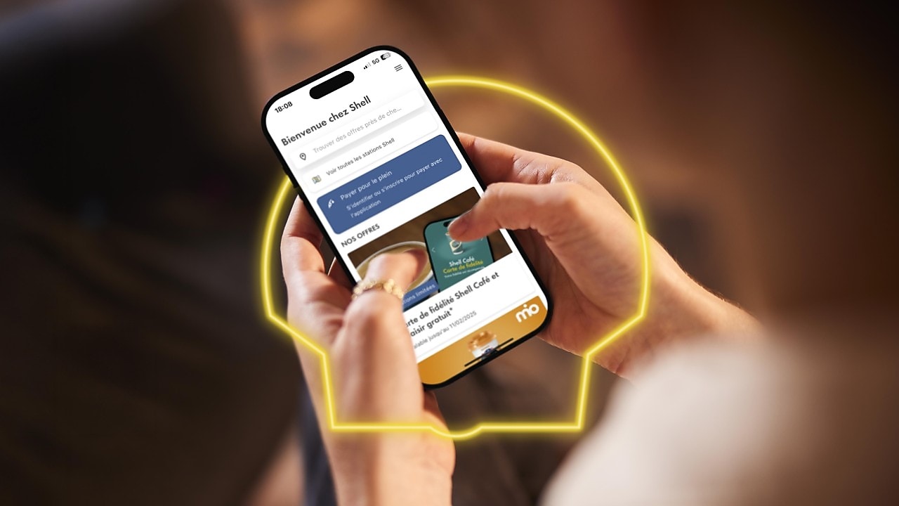 Une femme tient un téléphone avec l’application Shell ouverte et regarde les offres Shell Go+.